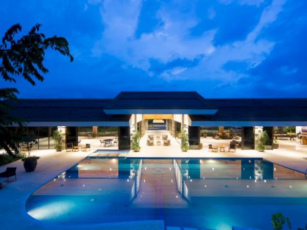 A luxurious resort at dusk, featuring an expansive swimming pool with ambient lighting, surrounded by elegant seating areas and modern architecture.