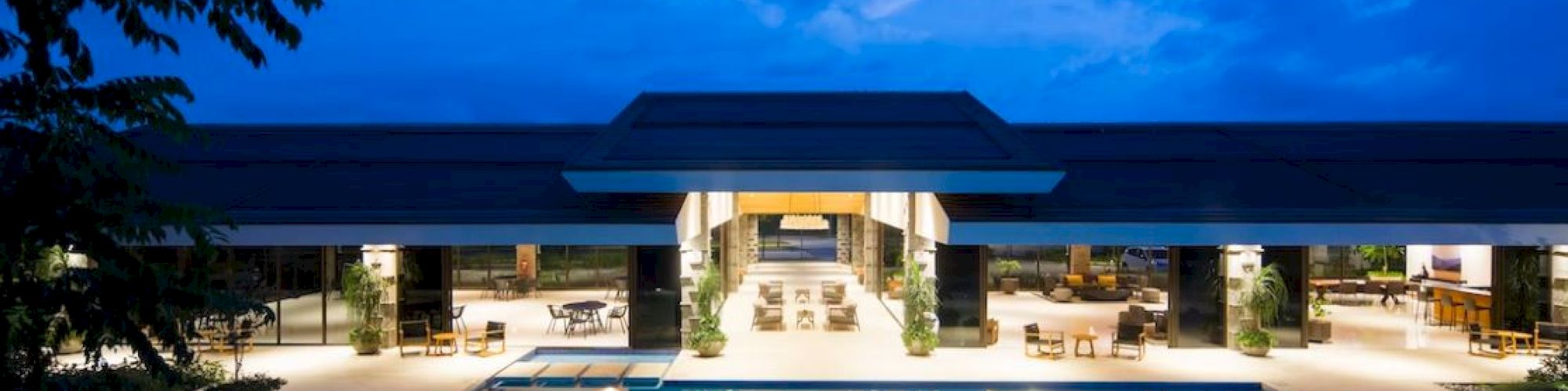 An illuminated luxury pool area at dusk, with a modern building in the background and outdoor seating arrangements.