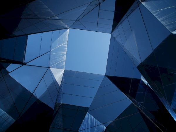 The image displays a perspective view of modern, reflective glass buildings forming an abstract geometric pattern against the sky.