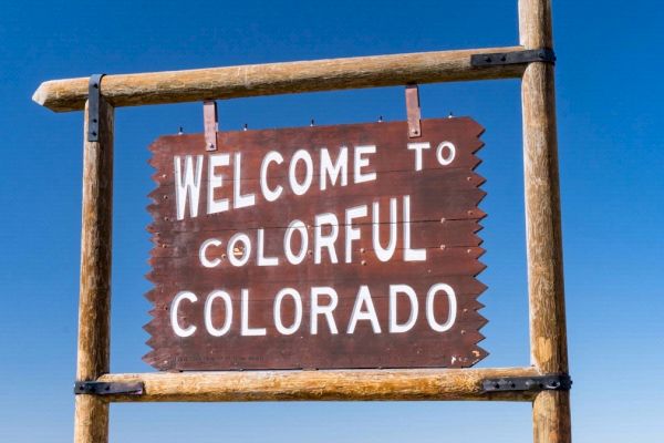 A wooden sign reads "Welcome to Colorful Colorado" against a clear blue sky, framed by wooden posts.