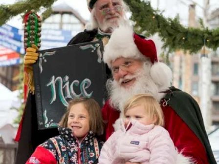 A person dressed as Santa Claus holds two young children, another figure holds a sign that says 