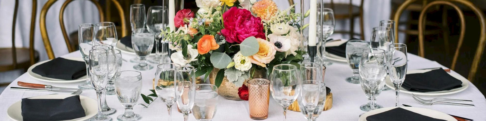 A round table is elegantly set with white tablecloth, black napkins, glassware, cutlery, and a floral centerpiece in a banquet setting ending the sentence.