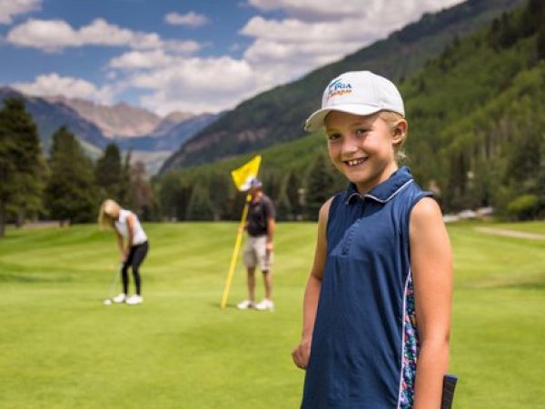 A young girl smiles in the foreground of a golf course with two people playing golf in the background, set against a mountainous landscape.