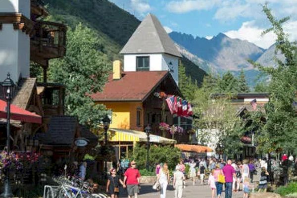 A bustling street with vibrant buildings, people walking, bicycles parked, and mountains in the background under a blue sky with fluffy clouds.