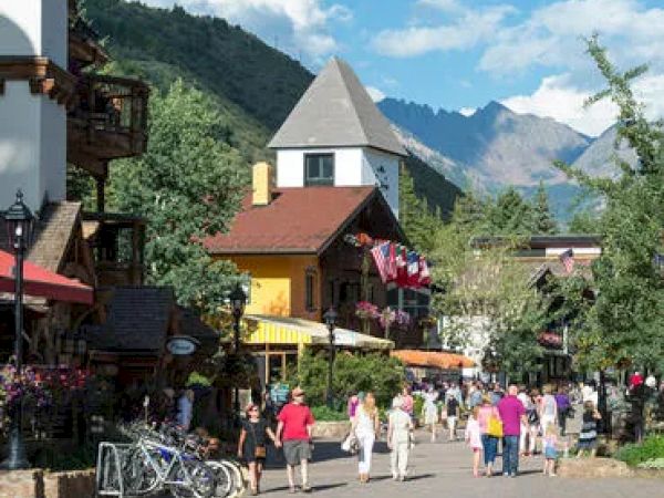 A bustling street with vibrant buildings, people walking, bicycles parked, and mountains in the background under a blue sky with fluffy clouds.