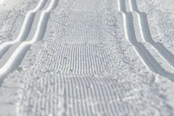 The image shows a freshly groomed cross-country skiing trail, featuring parallel grooves in the snow.