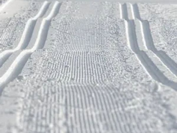 The image shows a freshly groomed cross-country skiing trail, featuring parallel grooves in the snow.