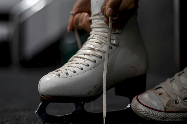 A person is tying the laces of a white ice skate on their foot, with the other foot wearing a white sneaker.