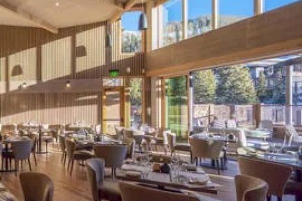 This image shows a well-lit restaurant with large windows, wooden floors and walls, and neatly arranged tables and chairs.