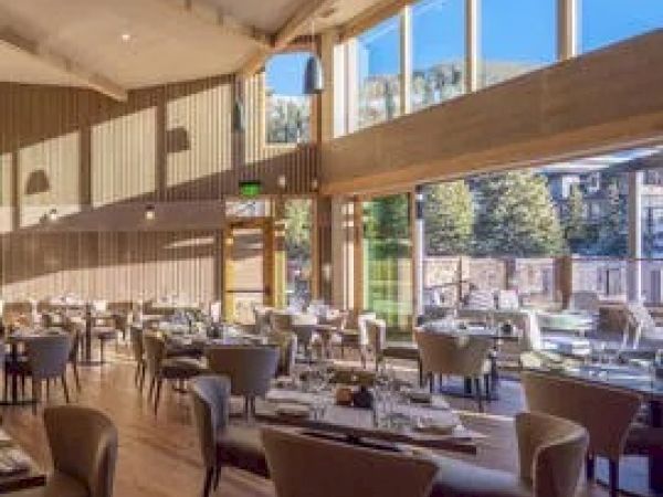 This image shows a well-lit restaurant with large windows, wooden floors and walls, and neatly arranged tables and chairs.