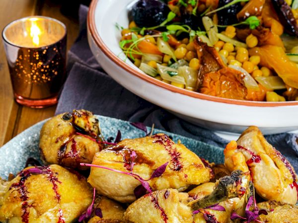 The image shows an arrangement of dishes: a plate of roasted chicken, a bowl of mixed vegetables, and decorative candles placed on a dining table.