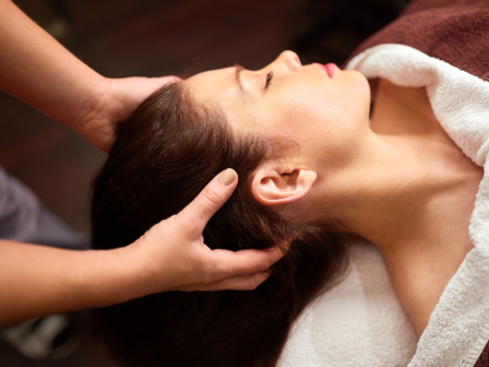 A person is receiving a relaxing head massage on a white towel while lying down.