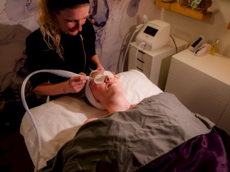 A person is receiving a facial treatment from a therapist using specialized equipment in a spa setting.