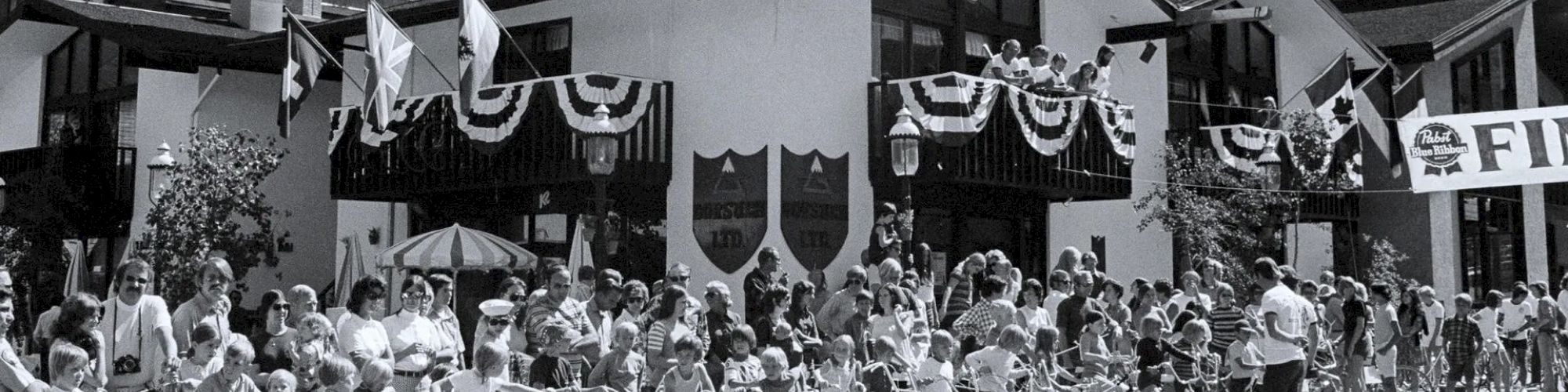 A group of people with bicycles is gathered in front of a decorated building with a clock tower, suggesting an event or celebration.