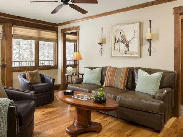 A cozy living room with a leather sofa, armchairs, wooden coffee table, wall art of a deer, and windows letting in natural light.