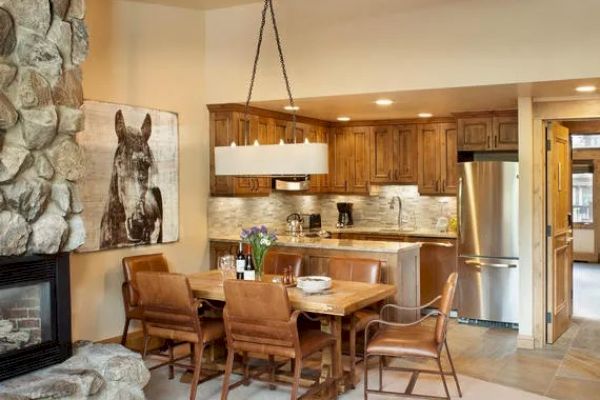 A cozy dining area with a wooden table, leather chairs, a stone fireplace, and a kitchen with wooden cabinets and stainless steel appliances.