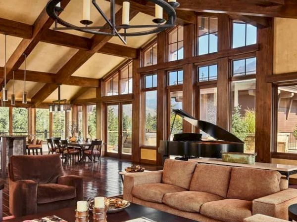 A spacious living room features large windows, wooden beams, a grand piano, a dining area, and cozy seating with a coffee table.