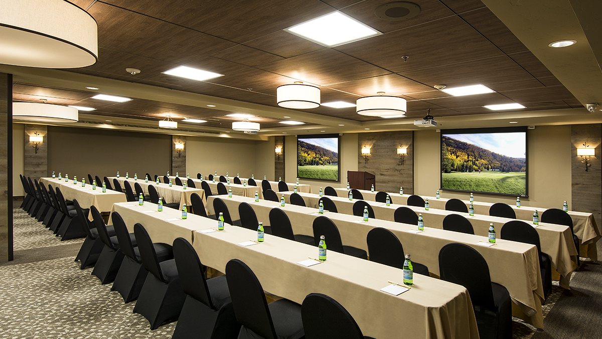 A conference room with rows of tables and chairs, each table having a small water bottle, and scenic pictures on the walls.