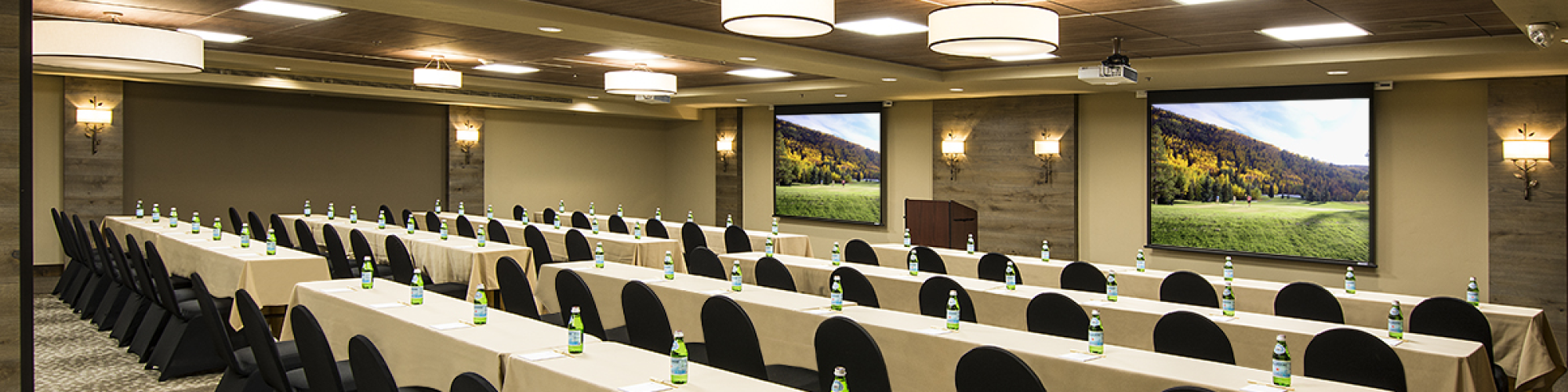 A conference room with rows of tables and chairs, each table having a small water bottle, and scenic pictures on the walls.