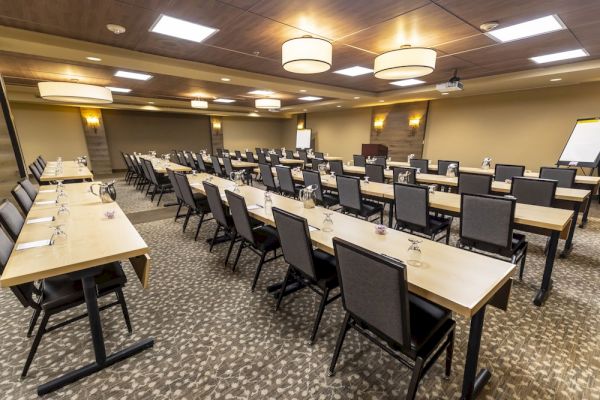 This image shows a conference room set up with rows of tables and chairs, prepared for a meeting or a seminar, well-lit with overhead lights.