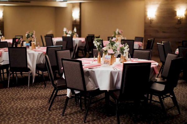 The image shows a banquet hall set up with decorated tables, flowers, and chairs, ready for an event or celebration, with dim lighting and elegant decor.