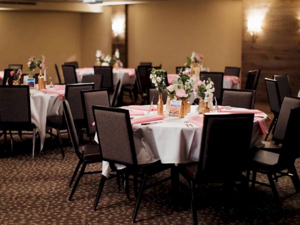 The image shows a banquet hall set up with decorated tables, flowers, and chairs, ready for an event or celebration, with dim lighting and elegant decor.