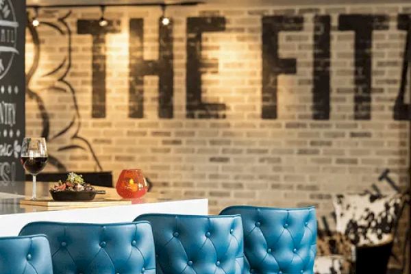 A stylish bar area with blue tufted stools, a countertop with wine and fruit, and a brick wall with 