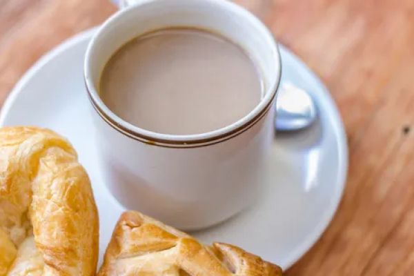 A white cup filled with coffee or tea on a plate, accompanied by two pastries on a wooden table.