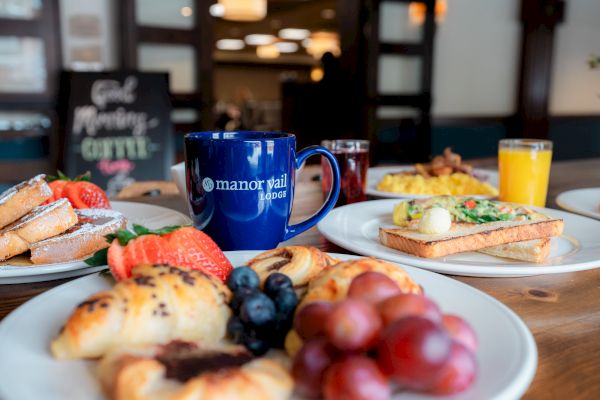 A breakfast spread with pastries, fruit, toast, eggs, a mug, and juice on a table.