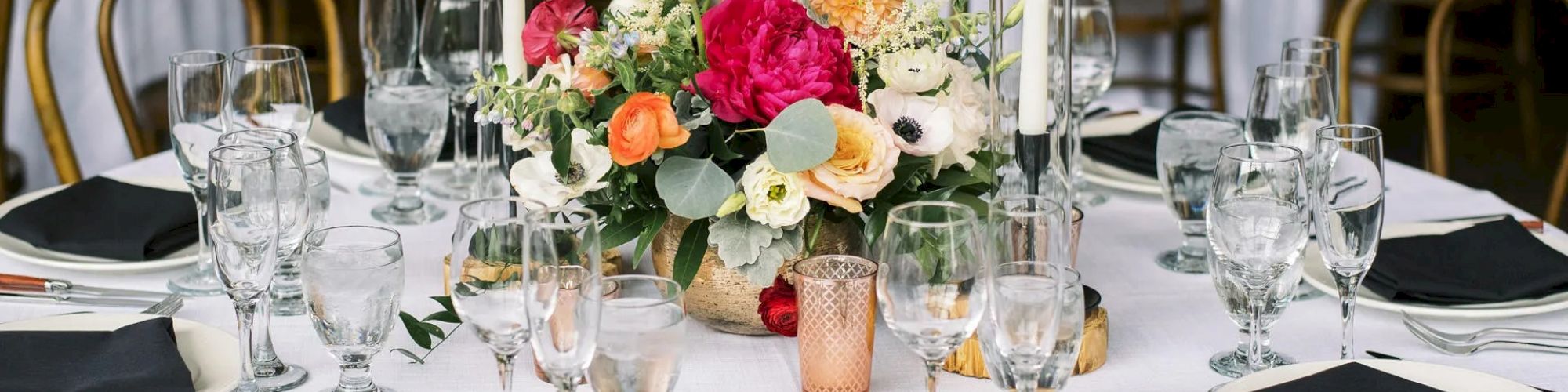 A beautifully set dinner table with black napkins, glassware, silverware, and a colorful floral centerpiece, ready for a formal event or wedding.