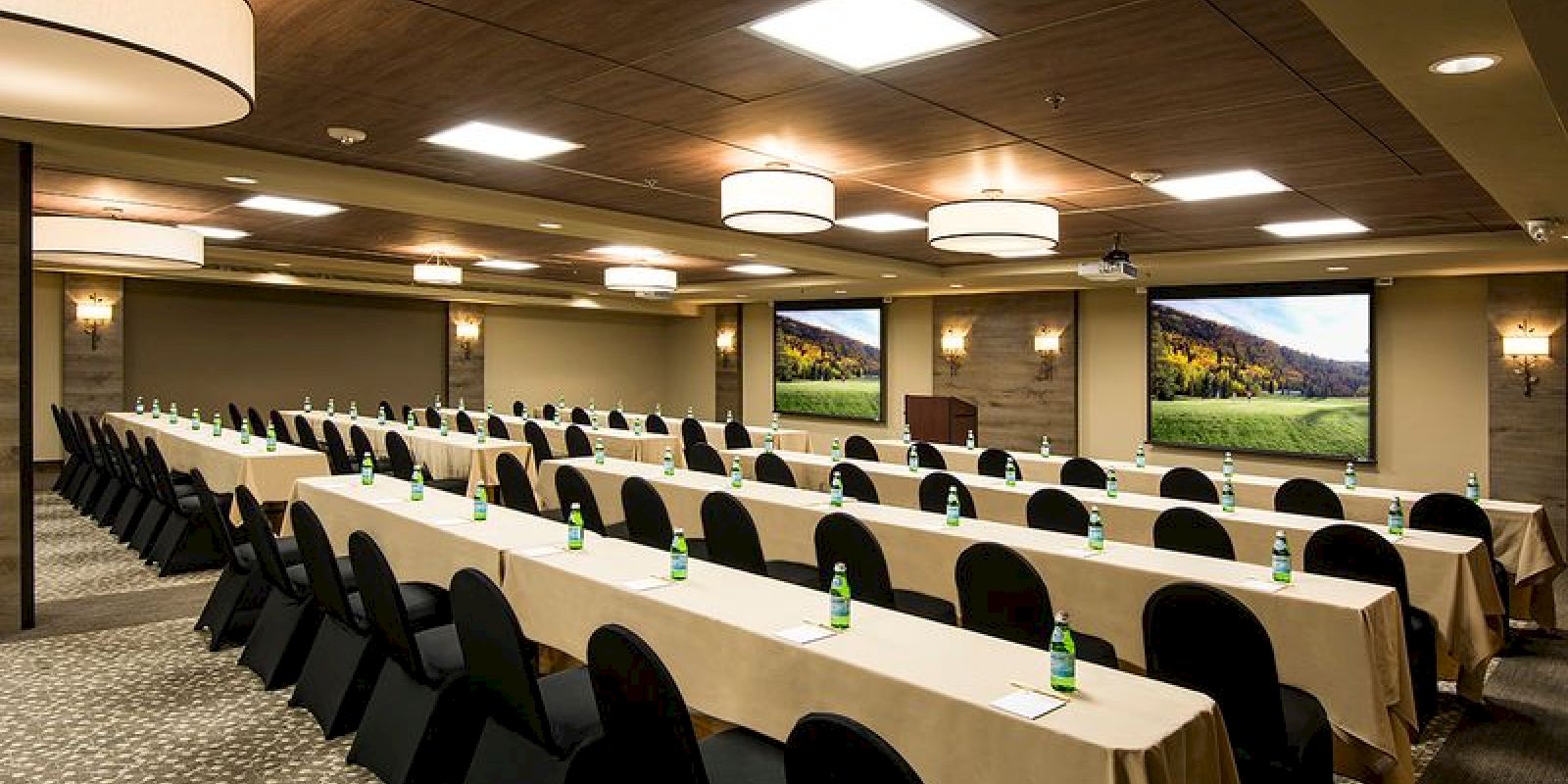 A conference room is set up with rows of tables and chairs, each table having a notepad and a water bottle. There is a podium at the front of the room.