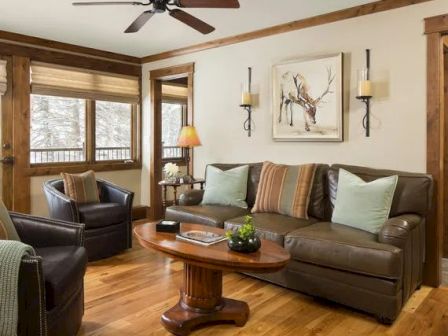 A cozy living room with a leather sofa, two armchairs, a wooden coffee table, and wall art of a deer. The space has earthy tones and natural lighting.