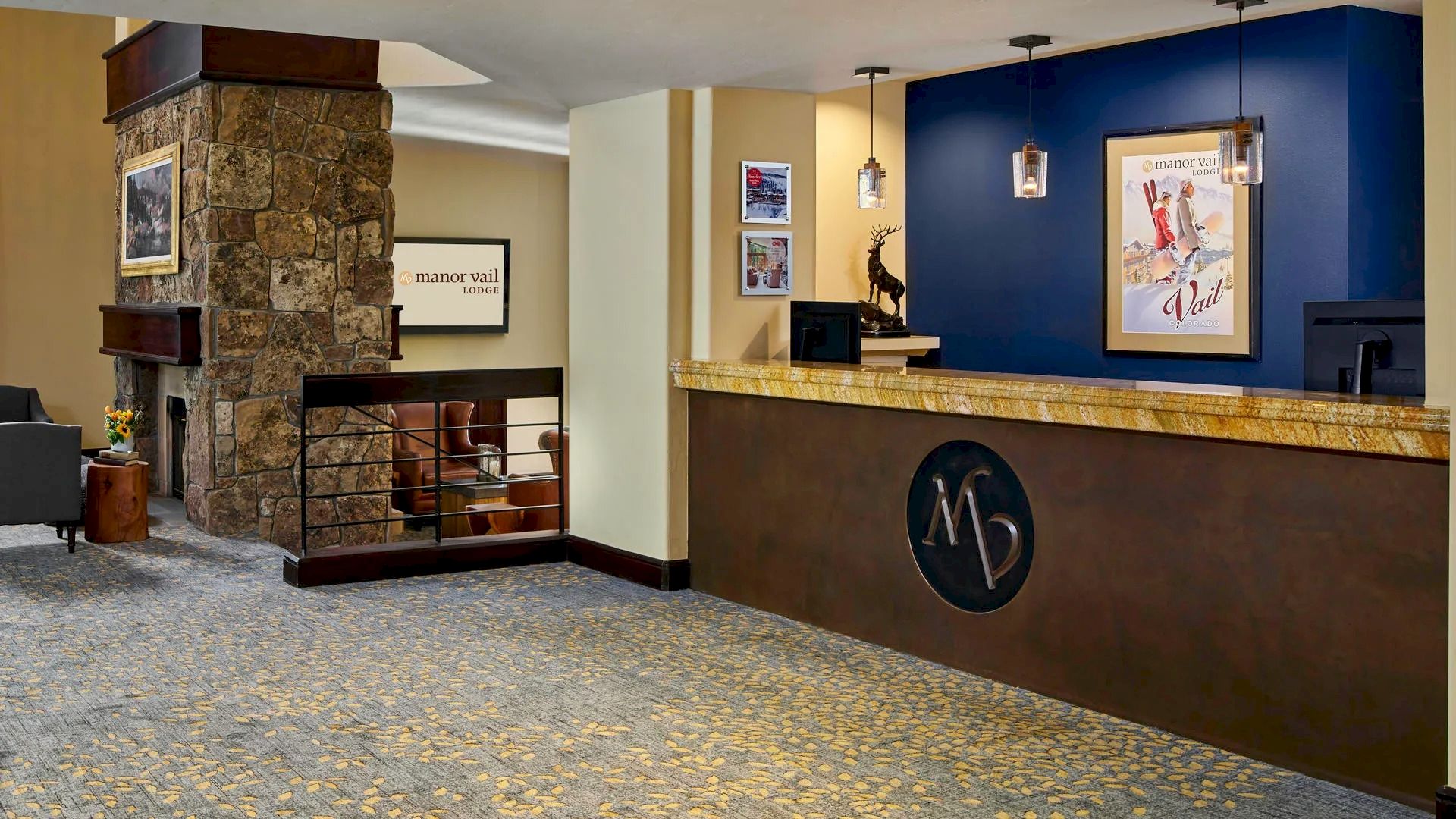 The image shows a hotel lobby with a reception desk, wall art, hanging lights, a stone pillar, and a seating area with chairs and a fireplace.