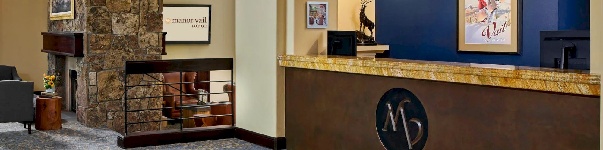 The image shows a hotel lobby with a reception desk, wall art, hanging lights, a stone pillar, and a seating area with chairs and a fireplace.