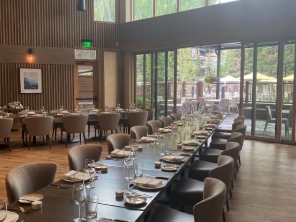 The image depicts a spacious, elegantly set dining area with large windows and modern lighting, offering a sophisticated ambiance.