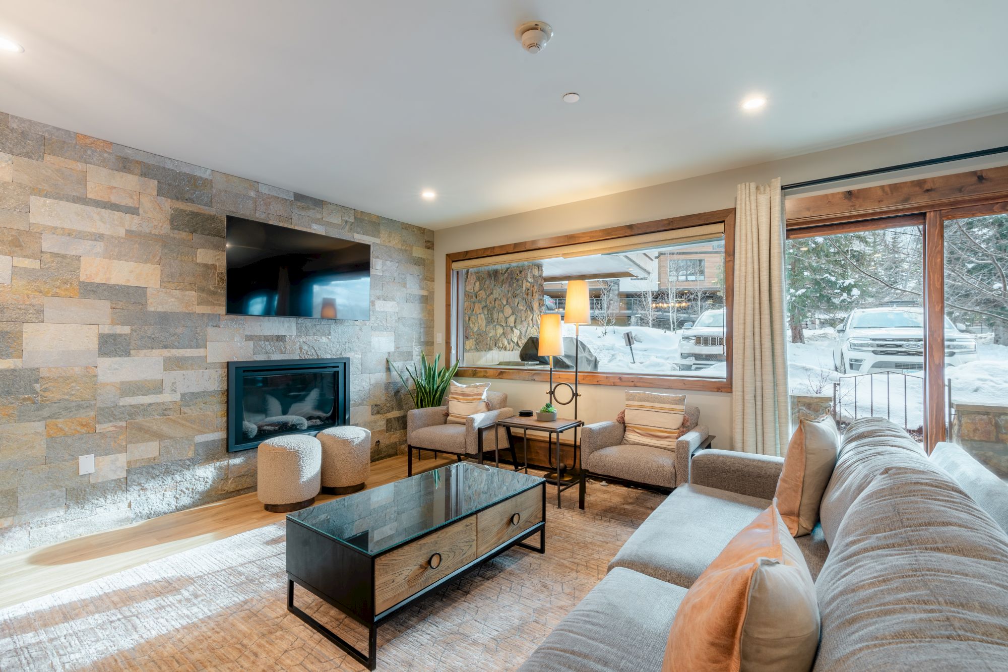 A cozy living room with a stone fireplace, large windows showcasing a snowy exterior, a sofa, armchairs, and a coffee table, ends the sentence.