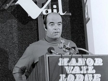 A man is speaking at a podium with a sign that reads 