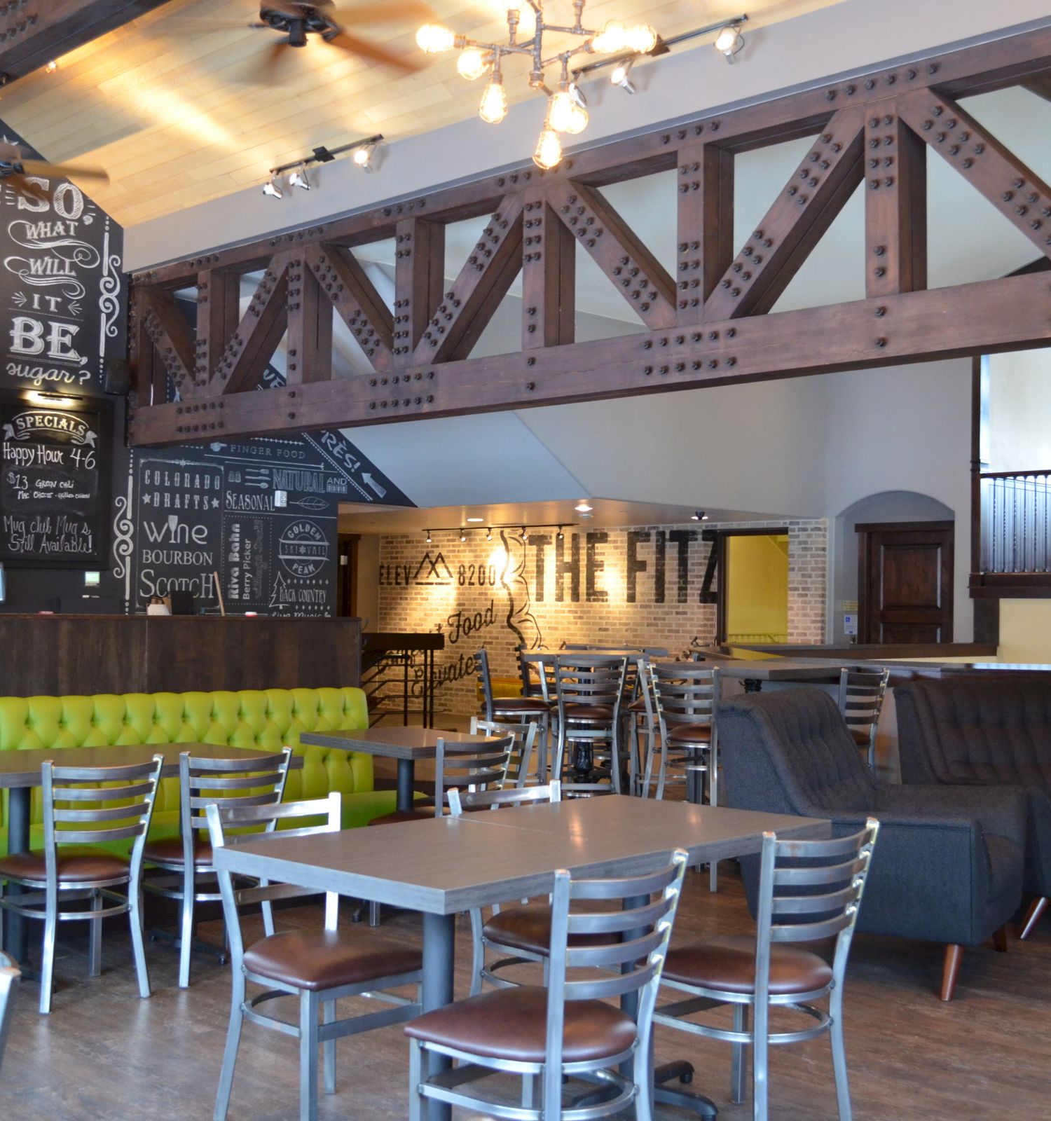 This image shows a cozy, modern cafe with metal and wooden accents, green booths, a chalkboard menu, and a fireplace.