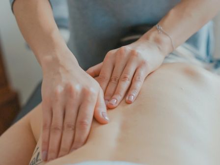 A person is receiving a back massage from a masseur or masseuse, who is applying pressure with their hands on the person's back.