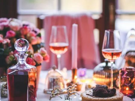 A beautifully set table with glass decanters, wine glasses filled with rosé, candles, and a floral centerpiece, creating a romantic ambiance.