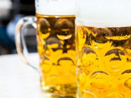 The image shows two large glass mugs filled with beer, each featuring a distinctive dimpled pattern.