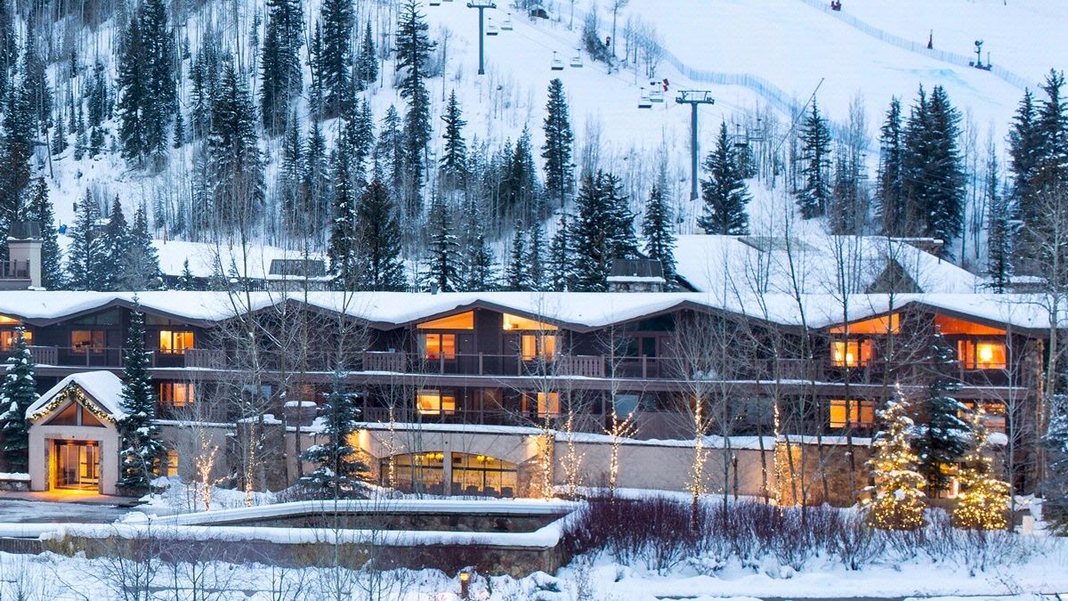 A cozy, illuminated lodge nestled in a snowy, forested mountain area, with ski lifts visible in the background.