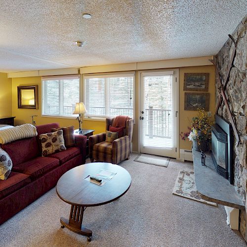 A cozy living room with a red sofa, stone fireplace, and TV, featuring a side table, armchair, and large windows leading to a balcony completed the decor.