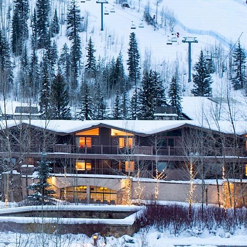 A cozy lodge nestled in a snowy landscape with evergreen trees, warm lights glowing, and ski lifts visible in the background ending the sentence.