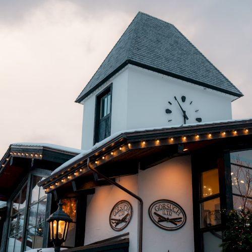 A charming building with a clock tower, illuminated lamps, and winter decorations, under a cloudy sky. The architecture suggests a cozy, festive atmosphere.