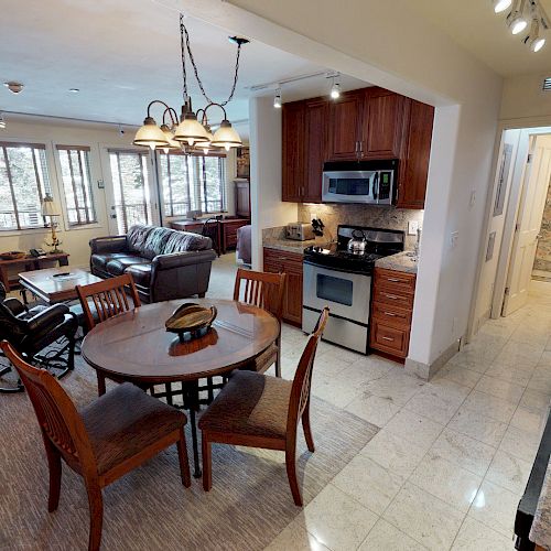 A cozy open-plan kitchen and living area with wooden cabinets, a dining table with four chairs, and a living room with a sofa and recliner chair.