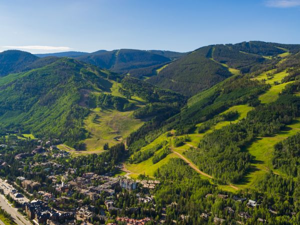 This image shows a scenic aerial view of a mountainous landscape with lush green hills, forests, and a small town nestled in a valley.