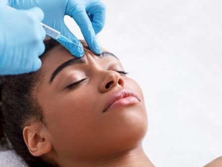 A person receiving a cosmetic injection on the forehead, administered by someone wearing blue gloves.