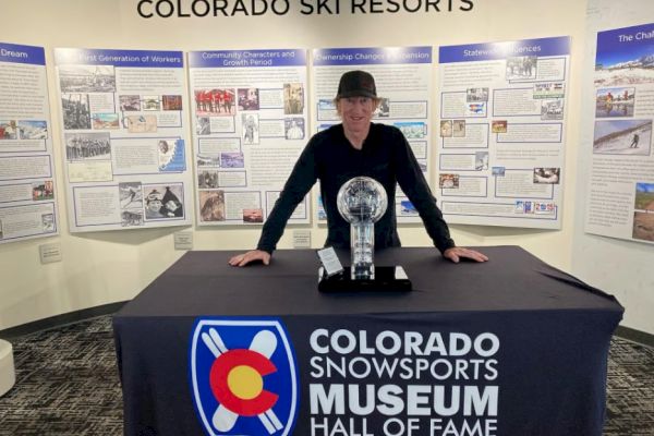 A person stands behind a table with a trophy at the Colorado Snowsports Museum Hall of Fame exhibition.