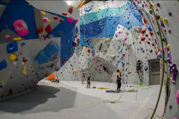 Indoor climbing gym with several people climbing walls, colorful holds, and a variety of climbing routes.